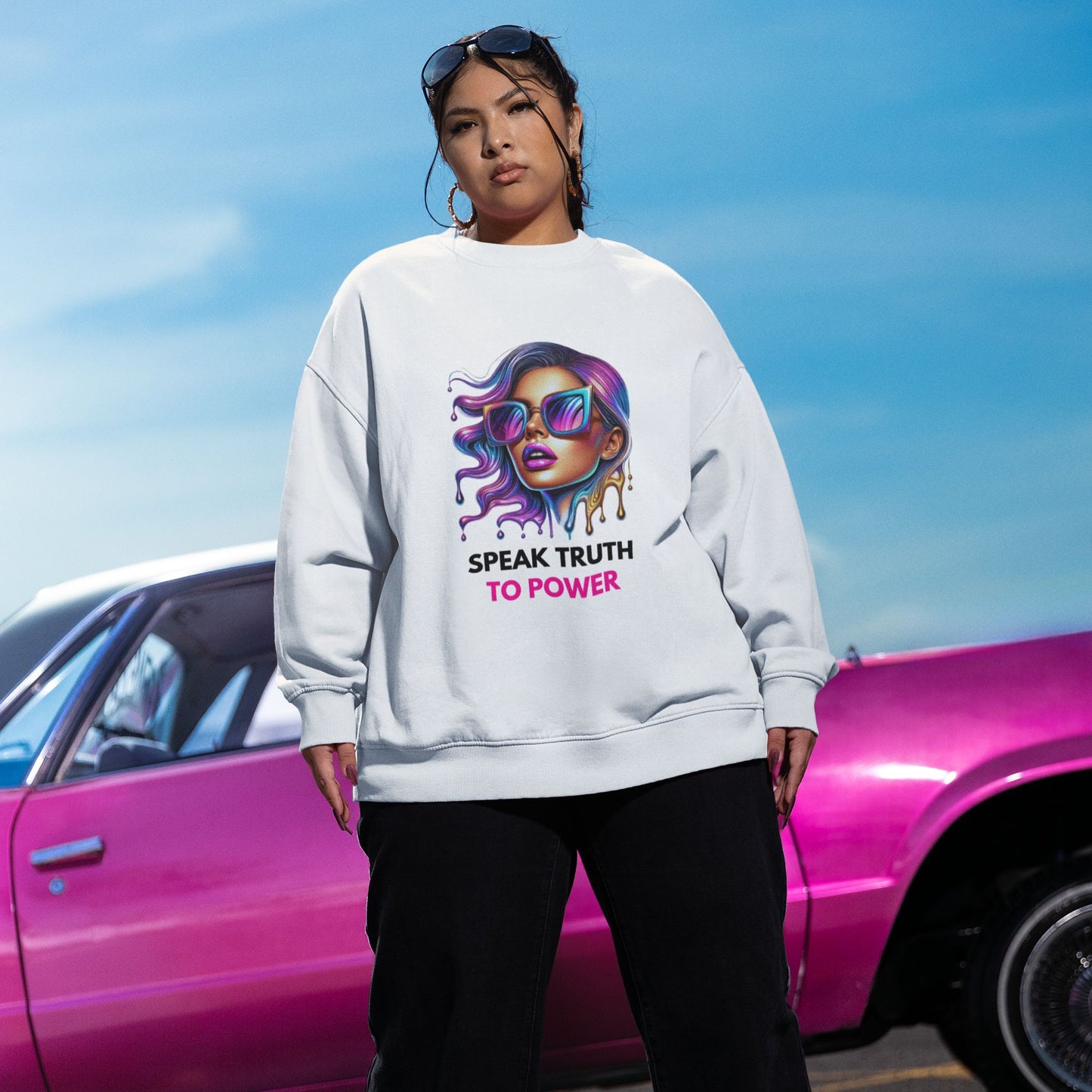Speak Truth to Power hers Sweatshirt in white, made from organic cotton. Female dark haired model showcasing sweatshirt in front view in front of a pink car.