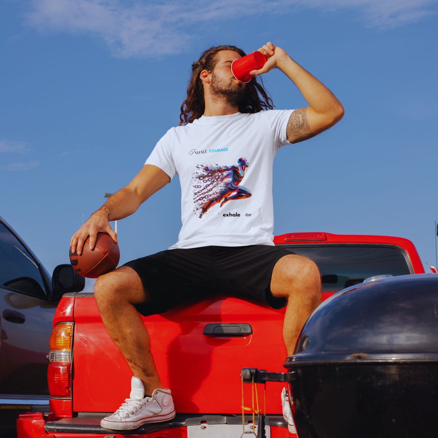Inhale courage exhale fear Shirt in white, made from organic cotton in conversion. Male model sitting on a truck wearing the shirt and drinking from a cup.