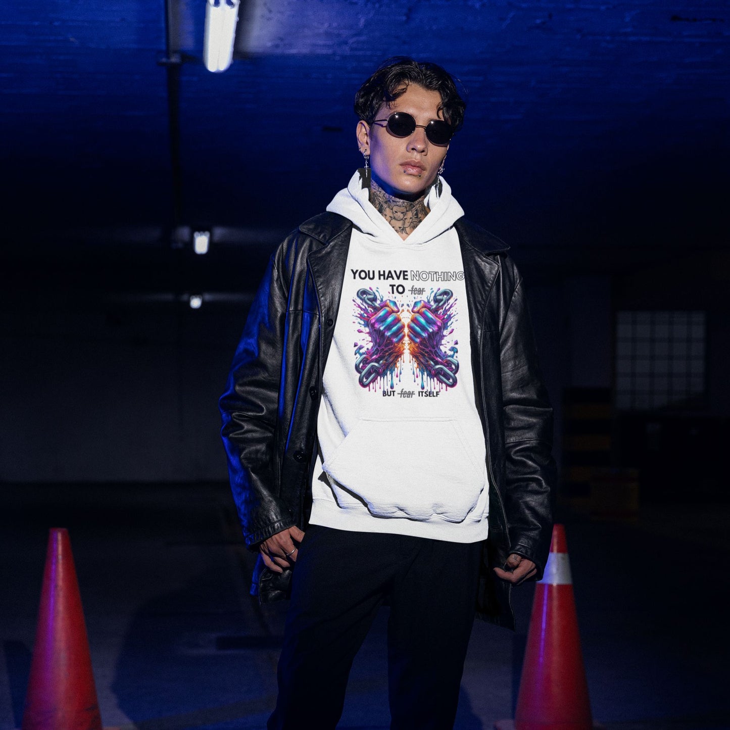 Nothing to fear Hoodie his in white, made from organic cotton. Model in sunglasses and a vegan leather jacket showcasing the hoodie in an underground setting.