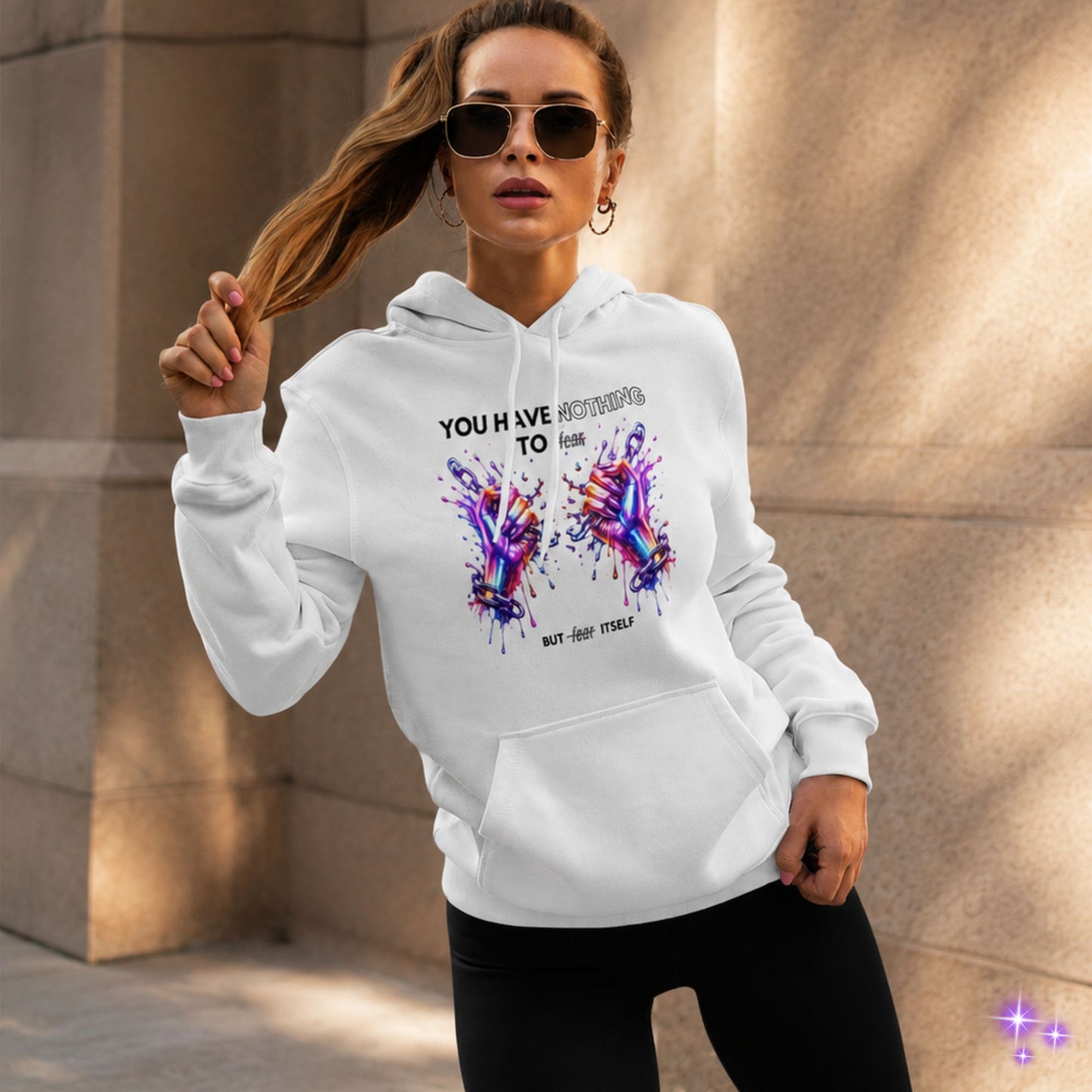 Woman wearing a white hoodie with colorful design and text, standing against a textured wall.