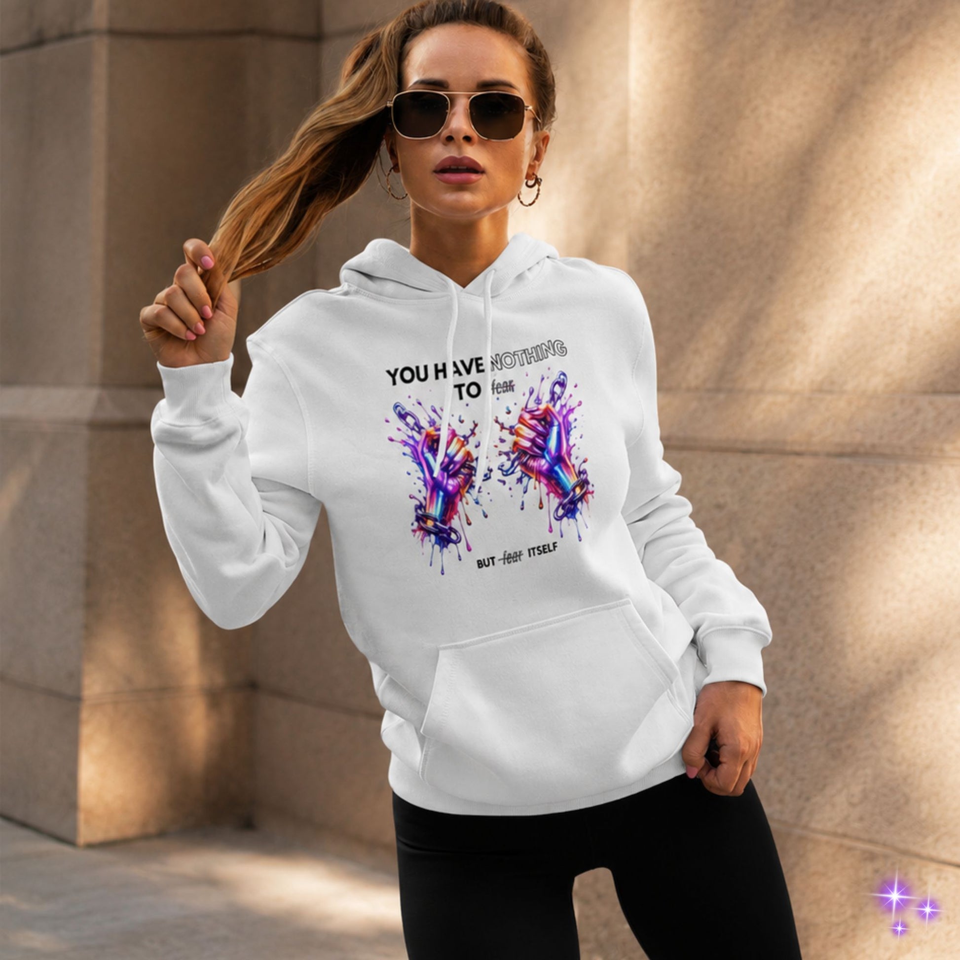 Woman wearing a white hoodie with colorful design and text, standing against a textured wall.
