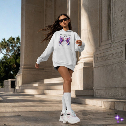 Woman in a white hoodie with butterfly design walking outdoors near classical architecture.