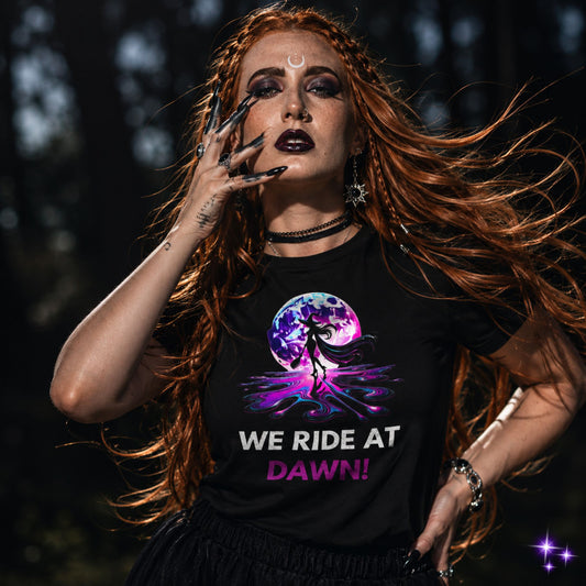 A person wearing a black t-shirt with a graphic design and text 'WE RIDE AT DAWN!' standing in a natural outdoor setting.