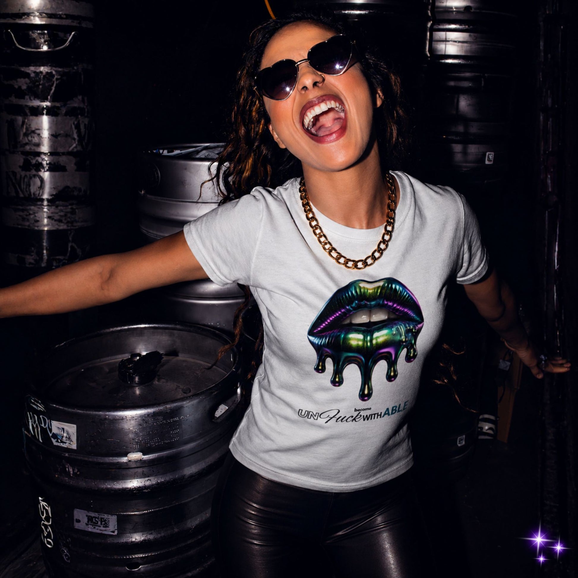 Person wearing a white t-shirt with a colorful graphic design, standing among stacked metal barrels.